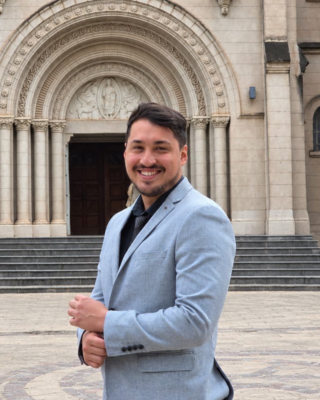 Martín Toledo frente a una catedral, de saco celeste, sonriendo